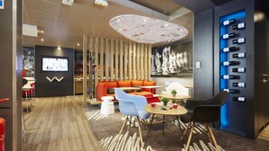 Un área de descanso moderna con un muro de listones de madera, un sofá rojo, sillas azules y una vitrina para vinos.