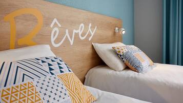 A hotel room with a wooden headboard displaying the name 'Réves'. The room has two beds with patterned bedding and decorative pillows.