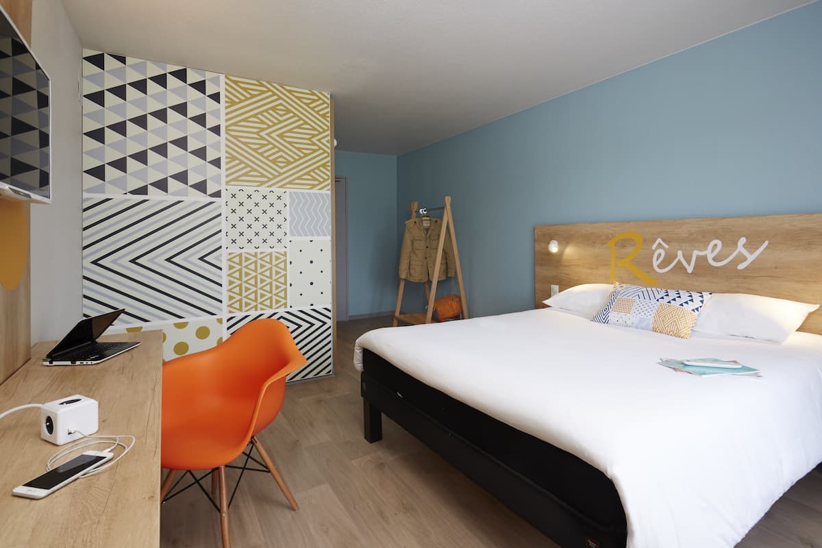 Ein Hotelzimmer mit einem Bett, einem Schreibtisch mit einem Laptop und einem orangefarbenen Sessel.