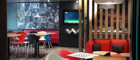 A modern interior with a wooden table, red seating, and a large screen displaying images.