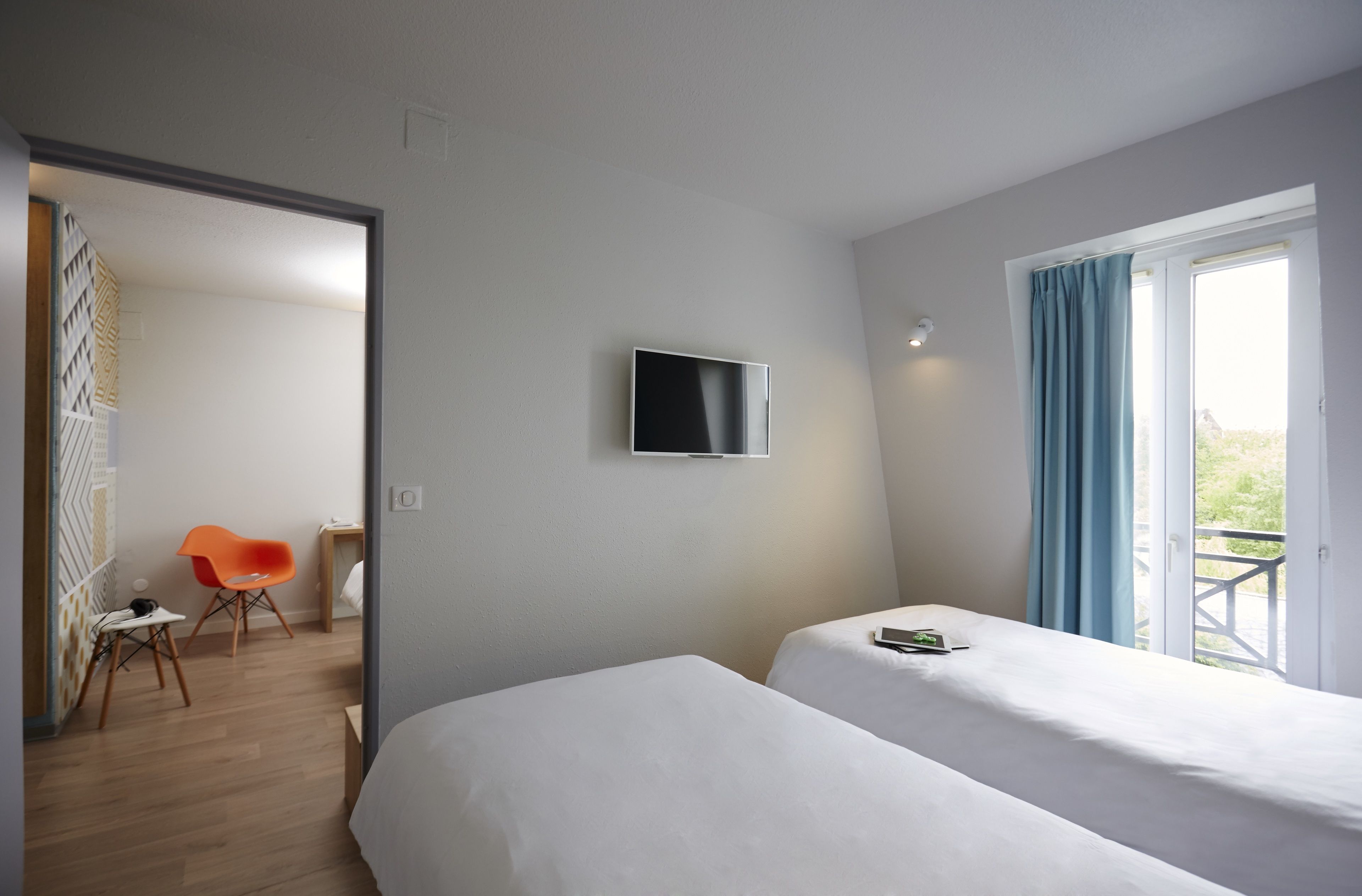 A hotel room with two beds, a TV on the wall, a window with curtains, a chair, and a desk.