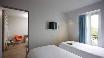 A hotel room with two beds, a TV on the wall, a window with curtains, a chair, and a desk.