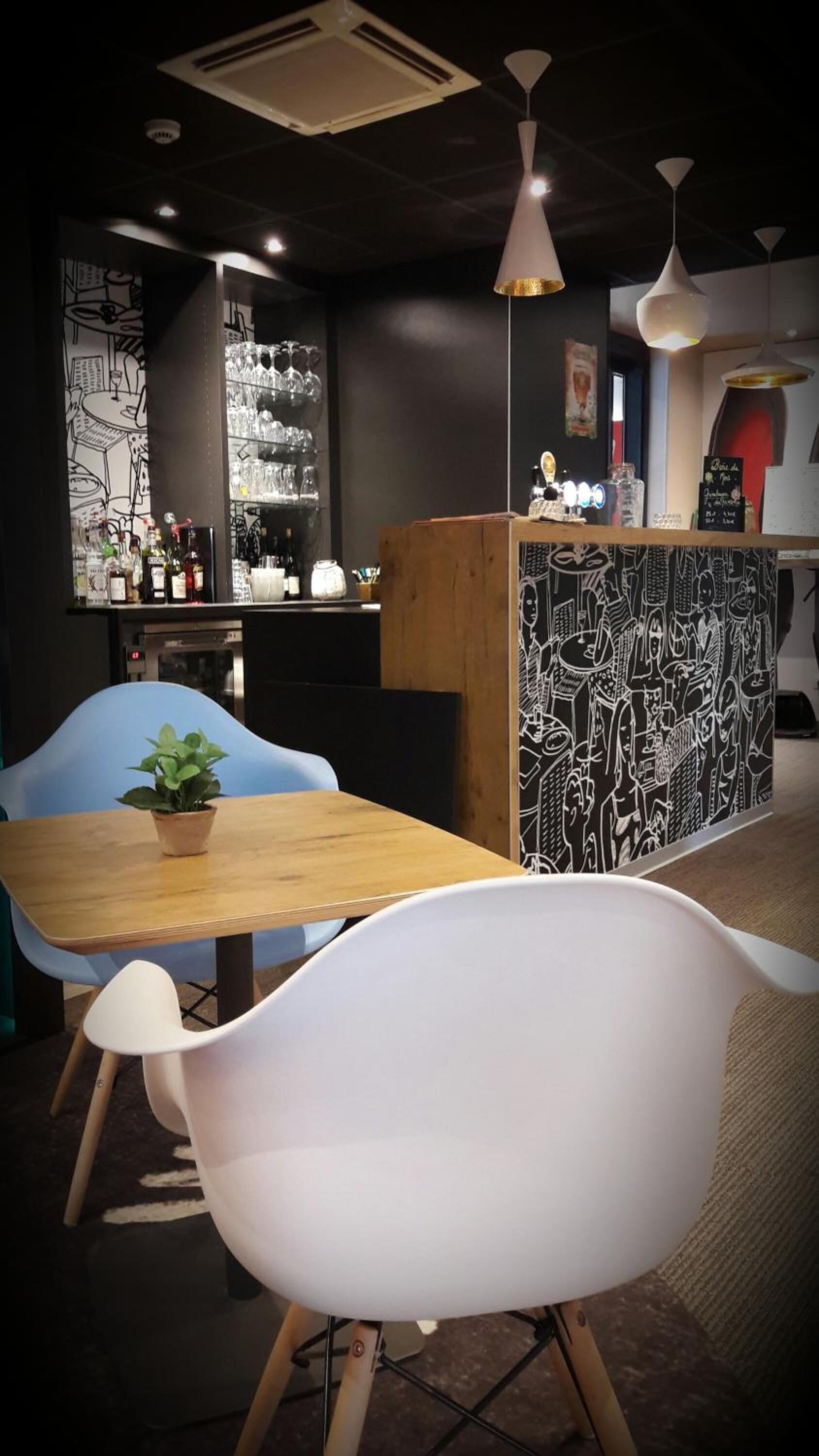 Een restaurantinterieur met een houten tafel, witte stoelen, een zwart-wit gestreept wand en een barruimte met flessen en glazen.