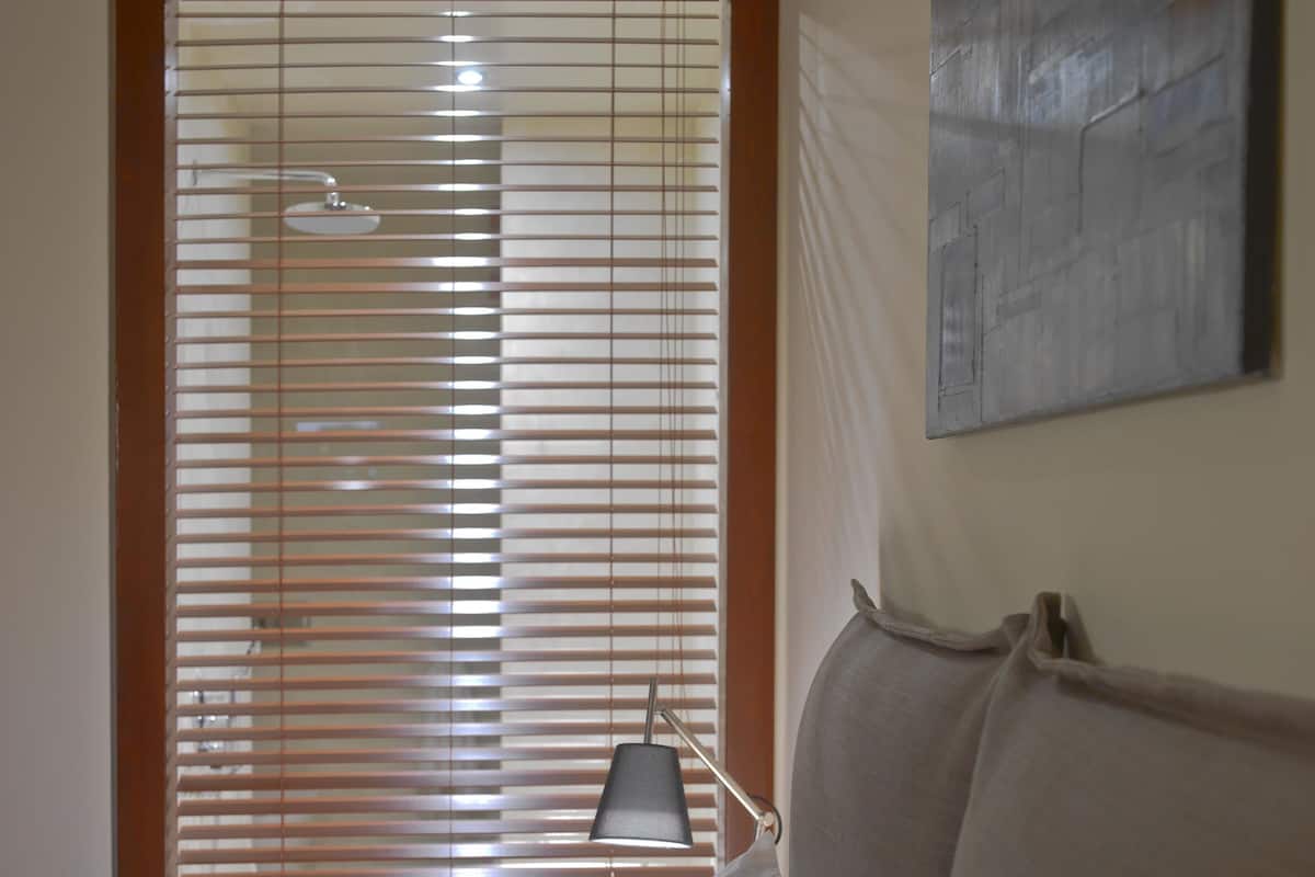 Ein Schlafzimmer mit einem Bett, einem Nachttisch, einer Lampe und einem Fenster mit Jalousien.