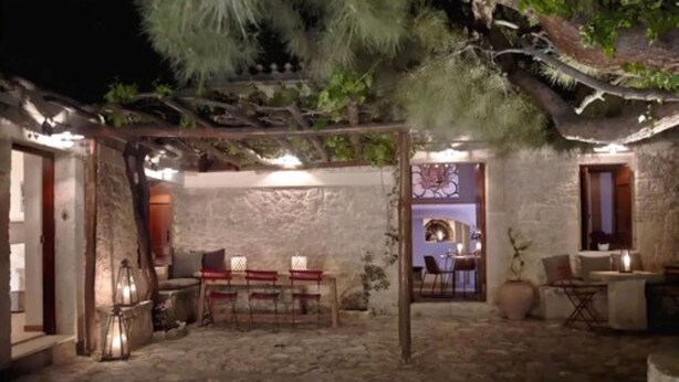 Une cour dallée de pierres, agrémentée d’une pergola en bois, d’un espace repas avec des chaises et d’une petite table.