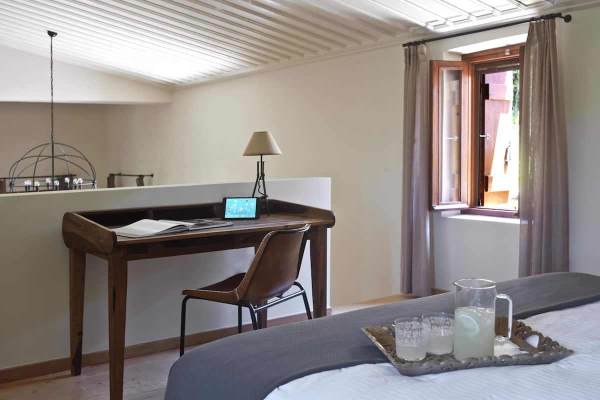 Ein Schlafzimmer mit einem Bett, einem Schreibtisch mit Stuhl, einer Lampe und einem Fenster mit Vorhängen.