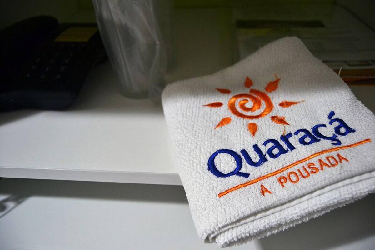A white towel with embroidered text and a sun design, placed on a white surface next to a keyboard and a plastic bag.