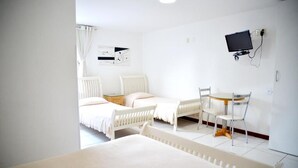 A hotel room with two beds, a desk, a chair, a TV, and a radiator. - Quaraçá Pousada (Maceió)