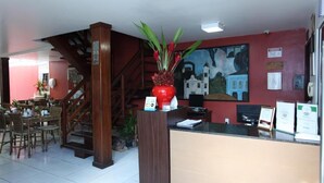 A reception area with a wooden staircase, a red vase with flowers, and a mural on the wall. - Quaraçá Pousada (Maceió)