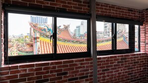 Una habitación con pared de ladrillo y ventana que ofrece vistas a un tejado chino tradicional y decoraciones coloridas.
