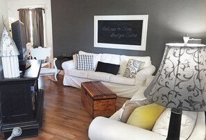 Ein Wohnzimmer mit einem weißen Sofa, einer Holzkiste, einem Vintage-Radio und einem Kreidetafel-Schild.