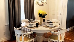 Comedor con una mesa redonda, sillas blancas, una araña y un florero con flores amarillas.