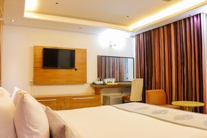 Una habitación de hotel con cama, escritorio, televisión y cortina.
