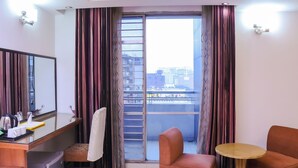 A hotel room with a balcony, a desk with a mirror, a chair, a small table, and curtains. - Hotel Afford Inn (Dhaka)