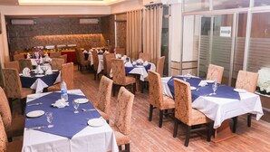 A dining area with multiple tables set for guests, featuring patterned chairs and a central buffet area. - Hotel Afford Inn (Dhaka)