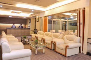 A hotel lobby with a reception desk, leather sofas, a glass coffee table, and a large window.