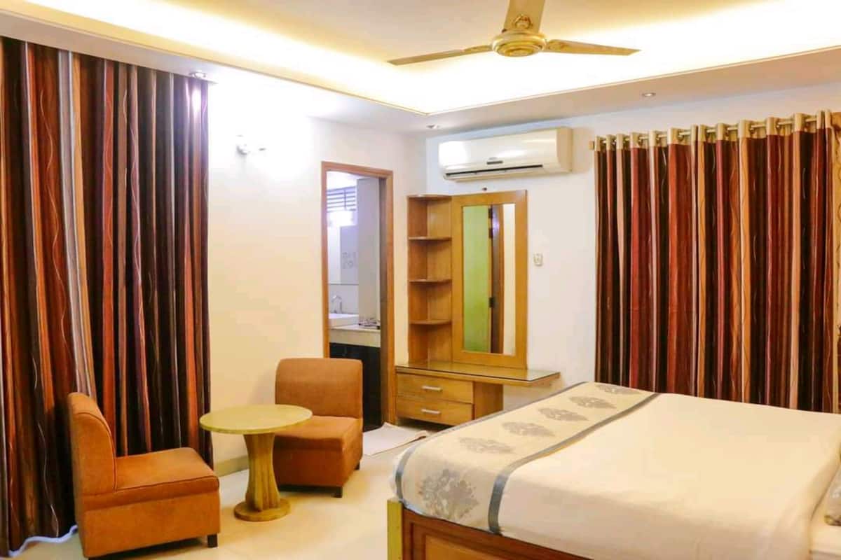 A hotel room with a bed, a small round table, a chair, a wardrobe, and a mirror.