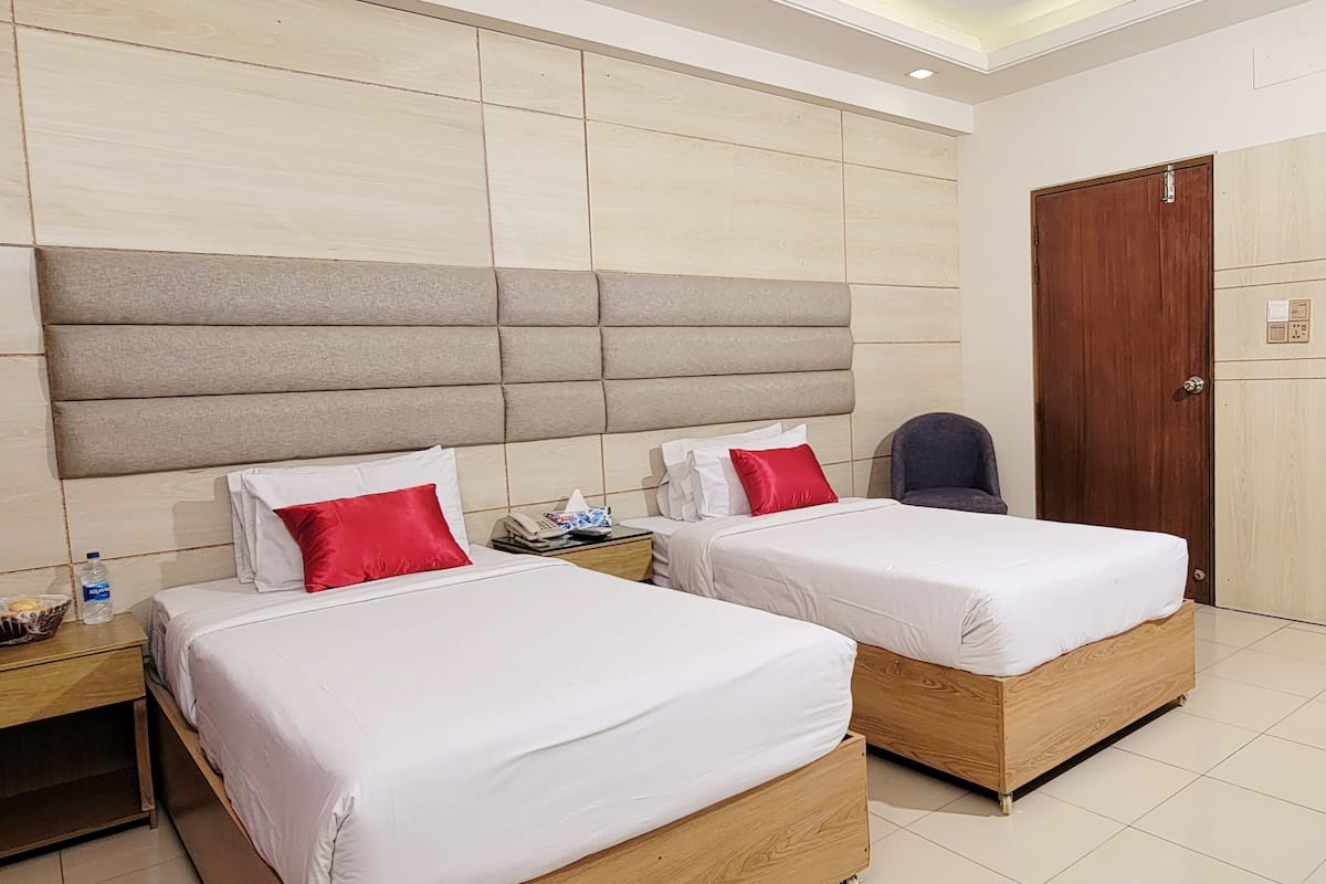 A hotel room with two single beds, a wooden headboard, a wardrobe, and a small table with toiletries.