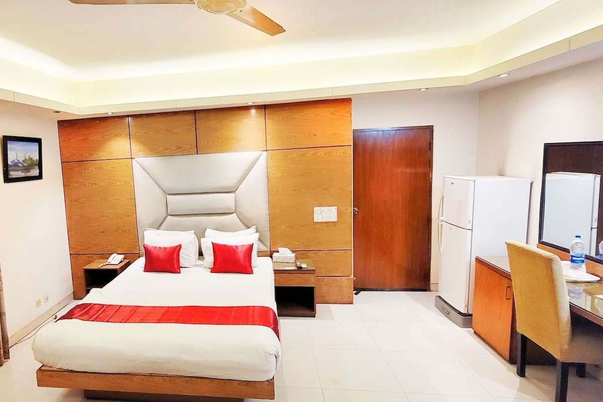 A hotel room with a bed, a desk, a chair, a wardrobe, and a mirror.