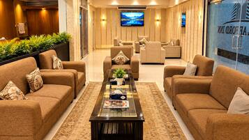A hotel lobby with sofas, a coffee table, a TV, and a reception desk.