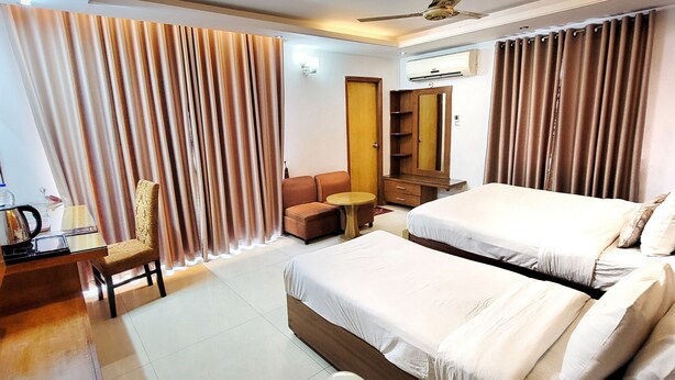 A hotel room with two beds, a desk with a chair, a small table, a wardrobe, and a ceiling fan. - Hotel Afford Inn (Dhaka)