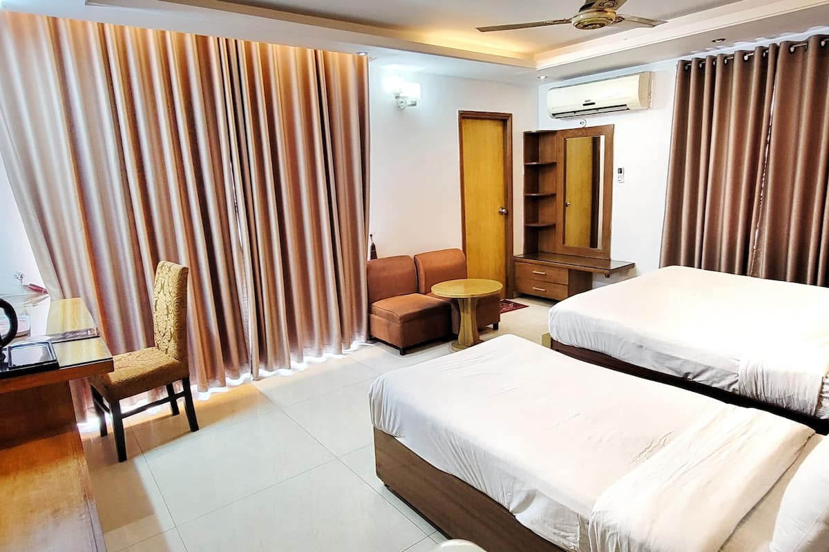 A hotel room with two beds, a desk with a chair, a small table, a wardrobe, and a ceiling fan.