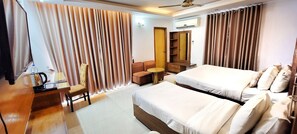 A hotel room with two beds, a desk with a chair, a small table, a wardrobe, and a ceiling fan. - Hotel Afford Inn (Dhaka)