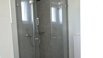 Eine Eckdusche mit Glastüren, ein weißes Waschbecken und eine Toilette.