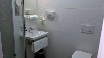 A bathroom with a glass shower enclosure, a white sink, a toilet, and a towel rack.