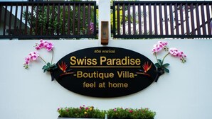 Een bord met 'Swiss Paradise Boutique Villa', versierd met decoratieve bloemen en een poort op de achtergrond.