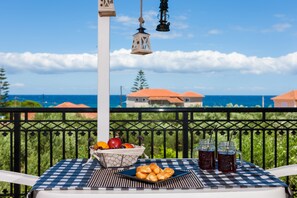 A balcony with a checkered tablecloth, a basket of fruits, a plate of pastries, and two mason jars of beverages. - Galatea (Zakynthos)