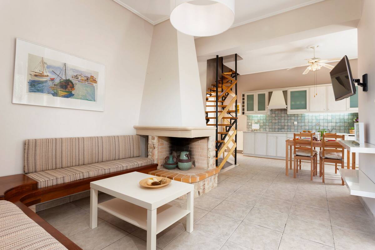 A modern living room with a fireplace, a dining area, and a kitchen in the background.