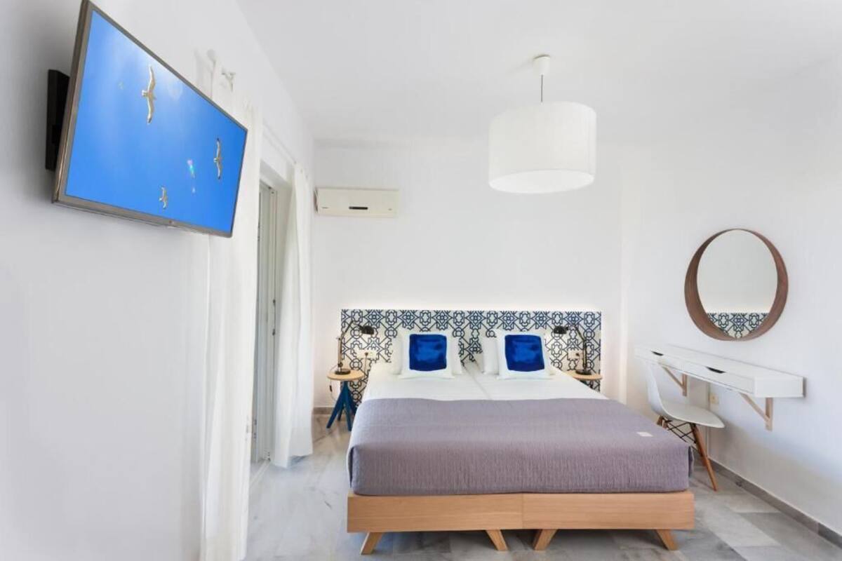 A modern bedroom with a bed, a TV, a desk, and a mirror.
