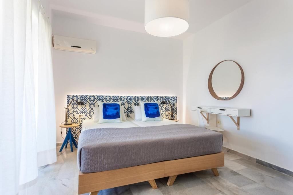 Un dormitorio moderno con cama, mesita de noche, lámpara y espejo en la pared.