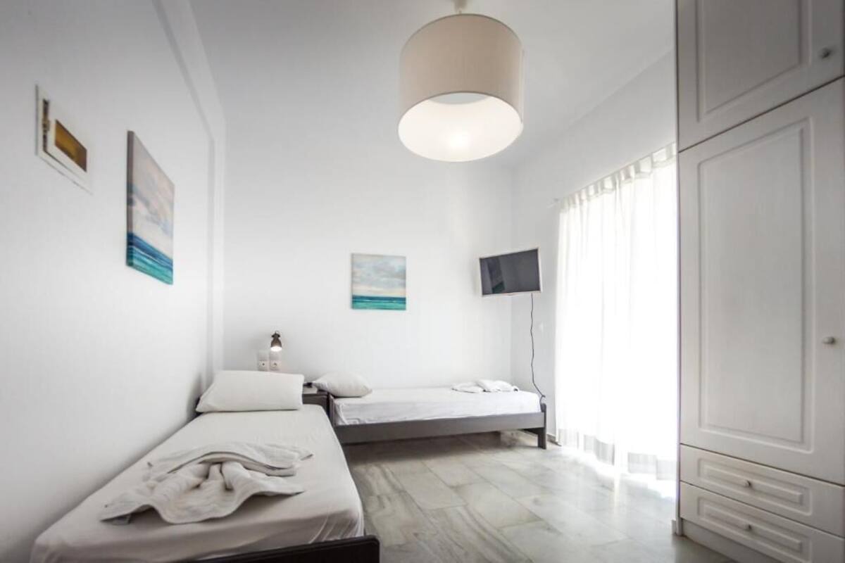 A minimalist bedroom with two single beds, a flat-screen TV, and a large wardrobe.