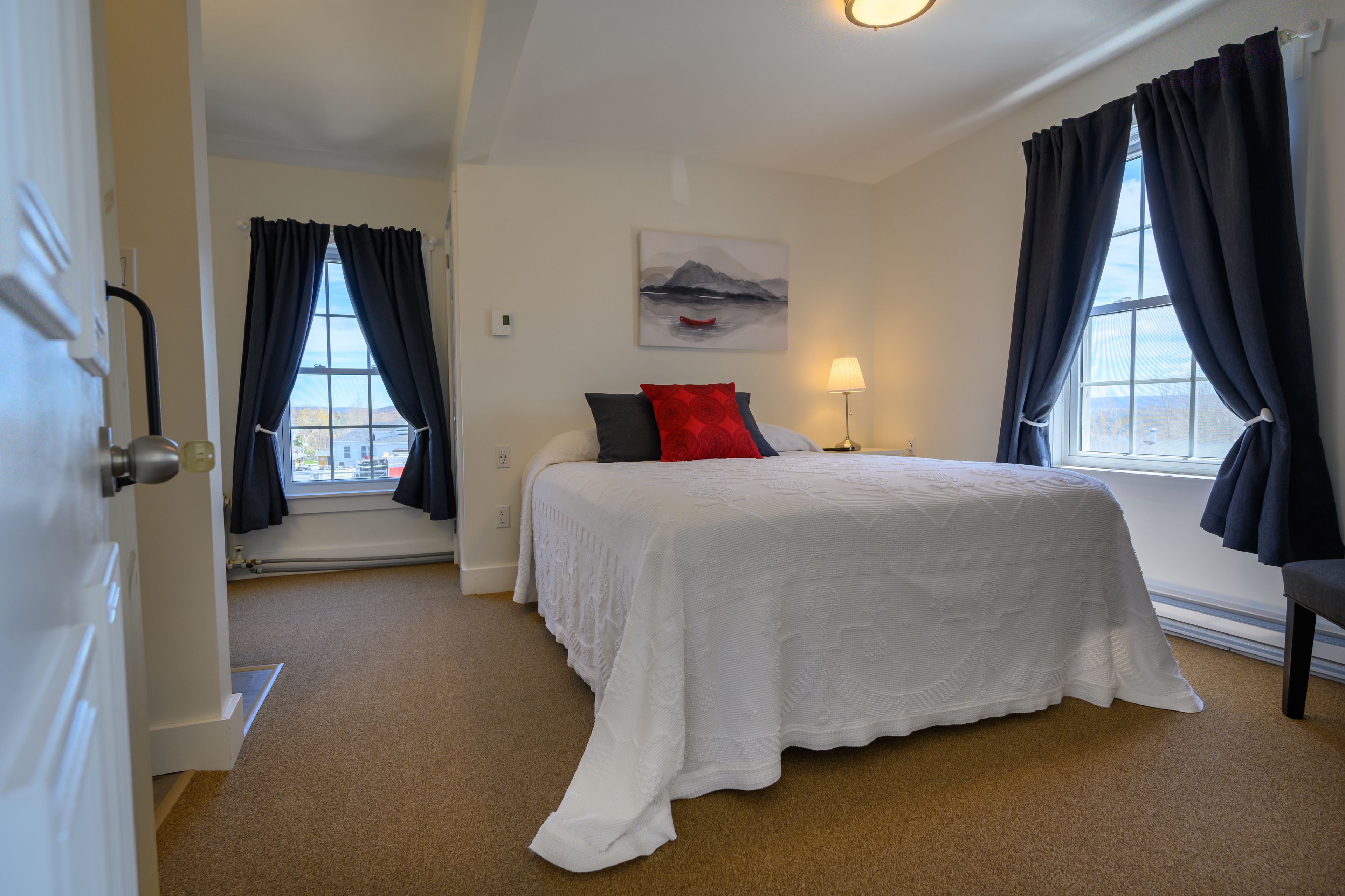 Een slaapkamer met een groot bed, een raam met gordijnen, een schilderij aan de muur en een lamp.