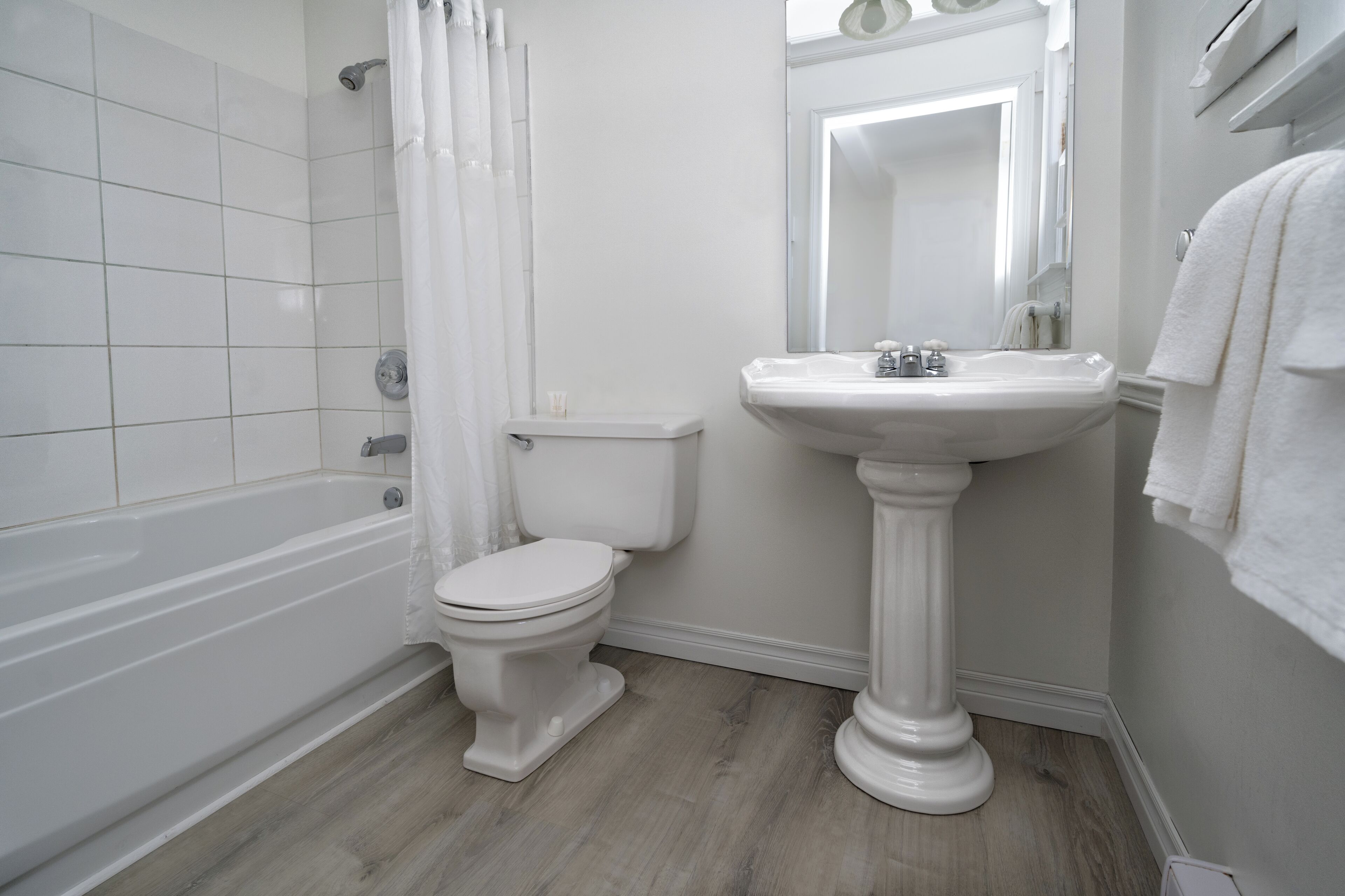 Un baño con bañera, inodoro y lavamanos pedestal.