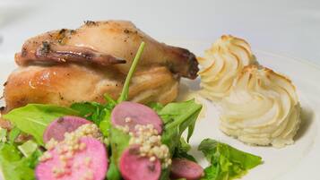 A plate with roasted chicken, mashed potatoes, and a salad with radishes and greens.