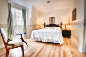 A bedroom with a large bed, two bedside tables with lamps, a chair, and a window with curtains.