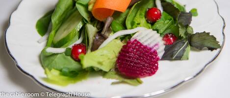 A plate of mixed greens salad with a carrot and a red fruit.