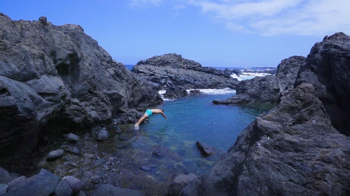 A rocky coastal area with clear water and a person in a blue swimsuit.