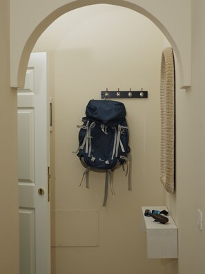 A hallway with a white door, a wall-mounted coat rack with a blue backpack, and a small white shelf with a remote control. - Coral Los Silos - Your Natural Accommodation Choice (Los Silos)