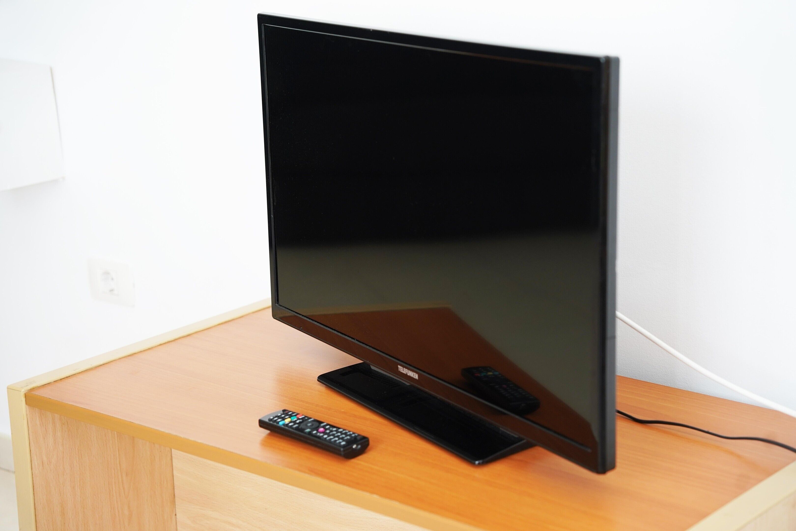 Un televisor de pantalla plana sobre una mesa de madera con un control remoto.