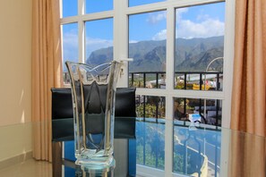 Un vase en verre transparent est posé sur une table en verre, et par la fenêtre, on peut admirer un paysage de montagnes.