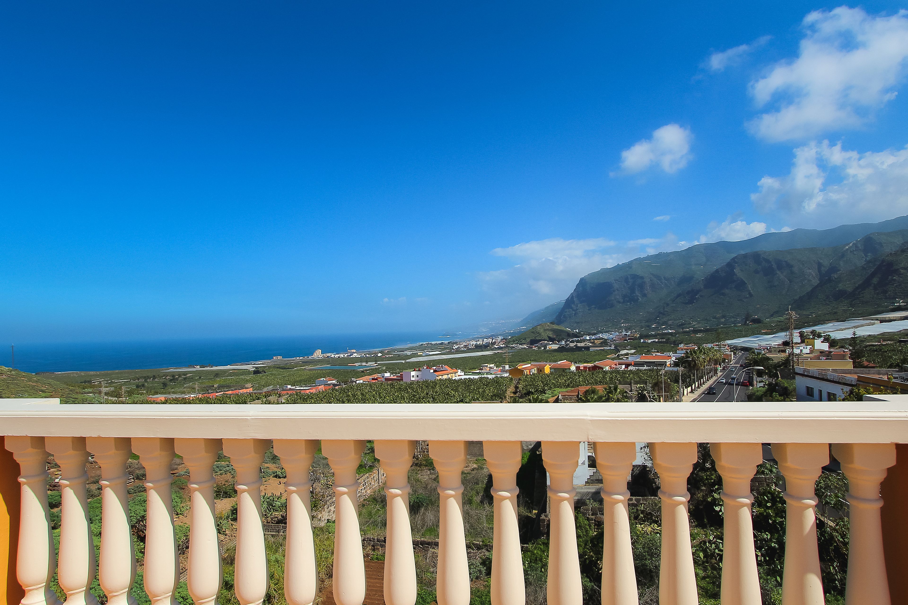 Ein Balkon mit Blick auf eine Küstenstadt, Berge und das Meer.