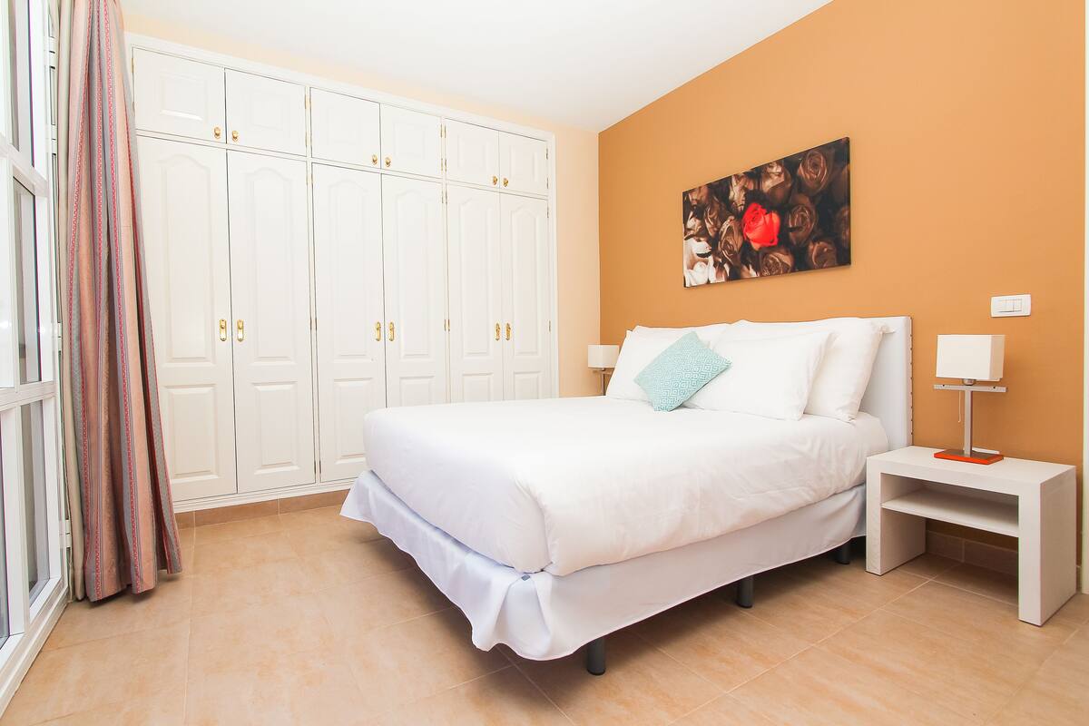 Un dormitorio con una cama, mesitas de noche, un armario y un cuadro en la pared.