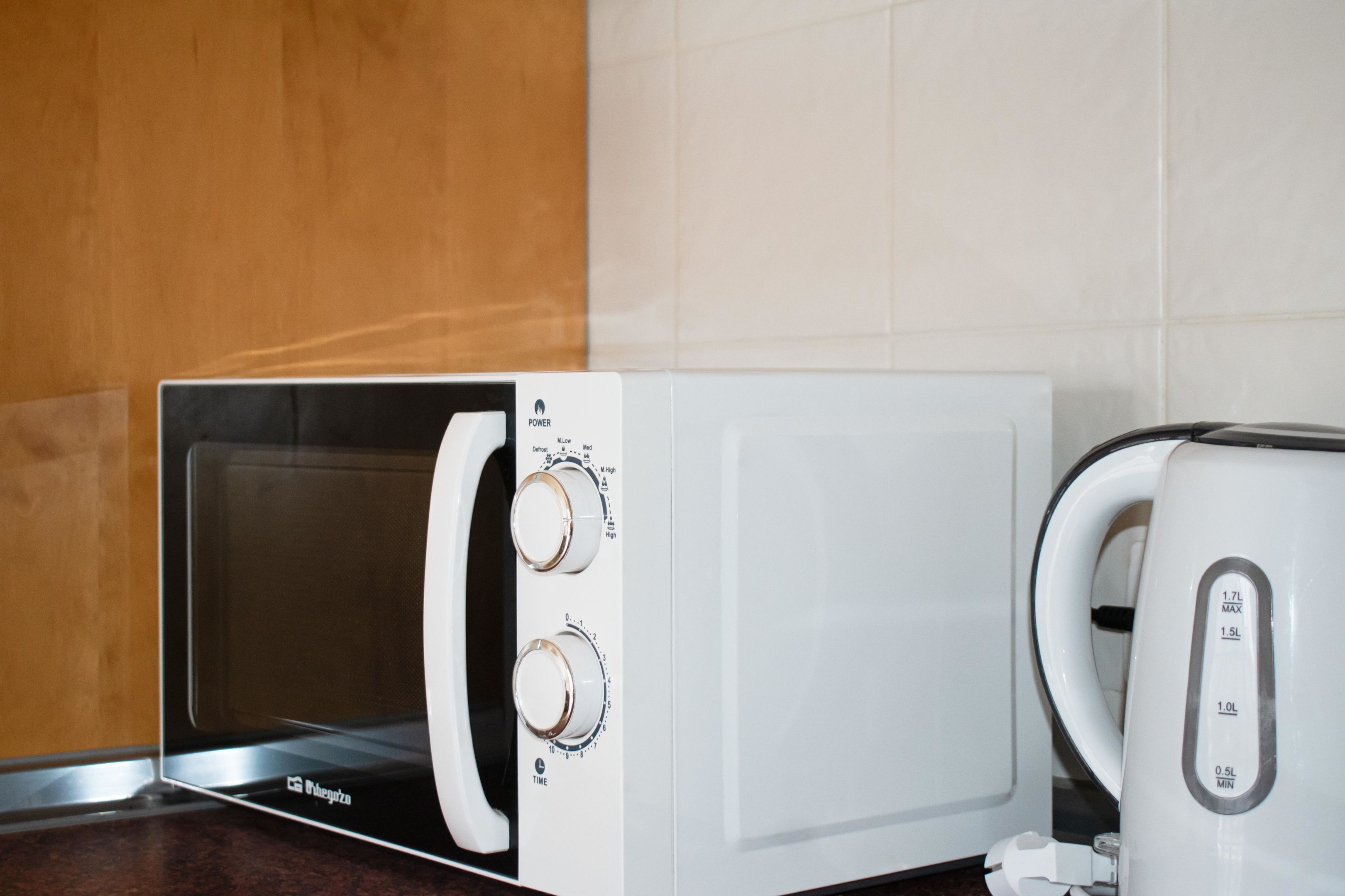 A microwave with a digital display and control panel, a kettle, and a toaster on a kitchen counter.