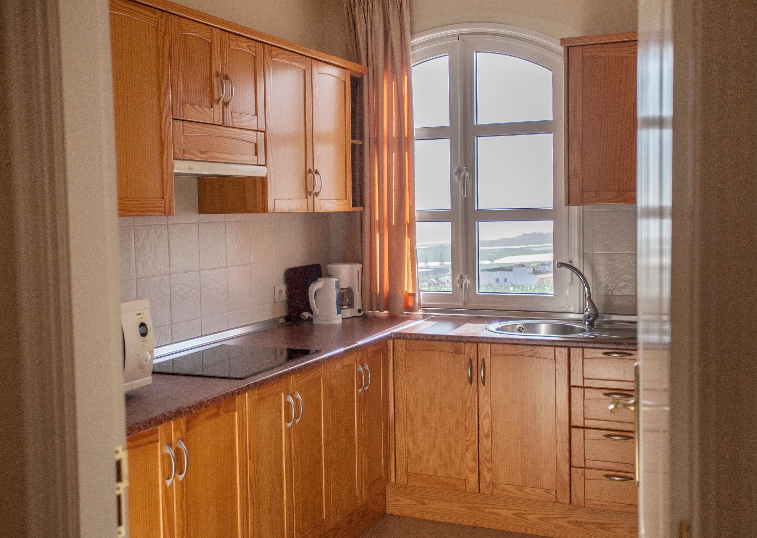 A kitchen with wooden cabinets, a window with curtains, a coffee maker, and a sink.