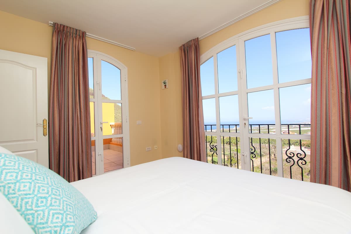 Un dormitorio con cama, puerta y balcón con vistas.