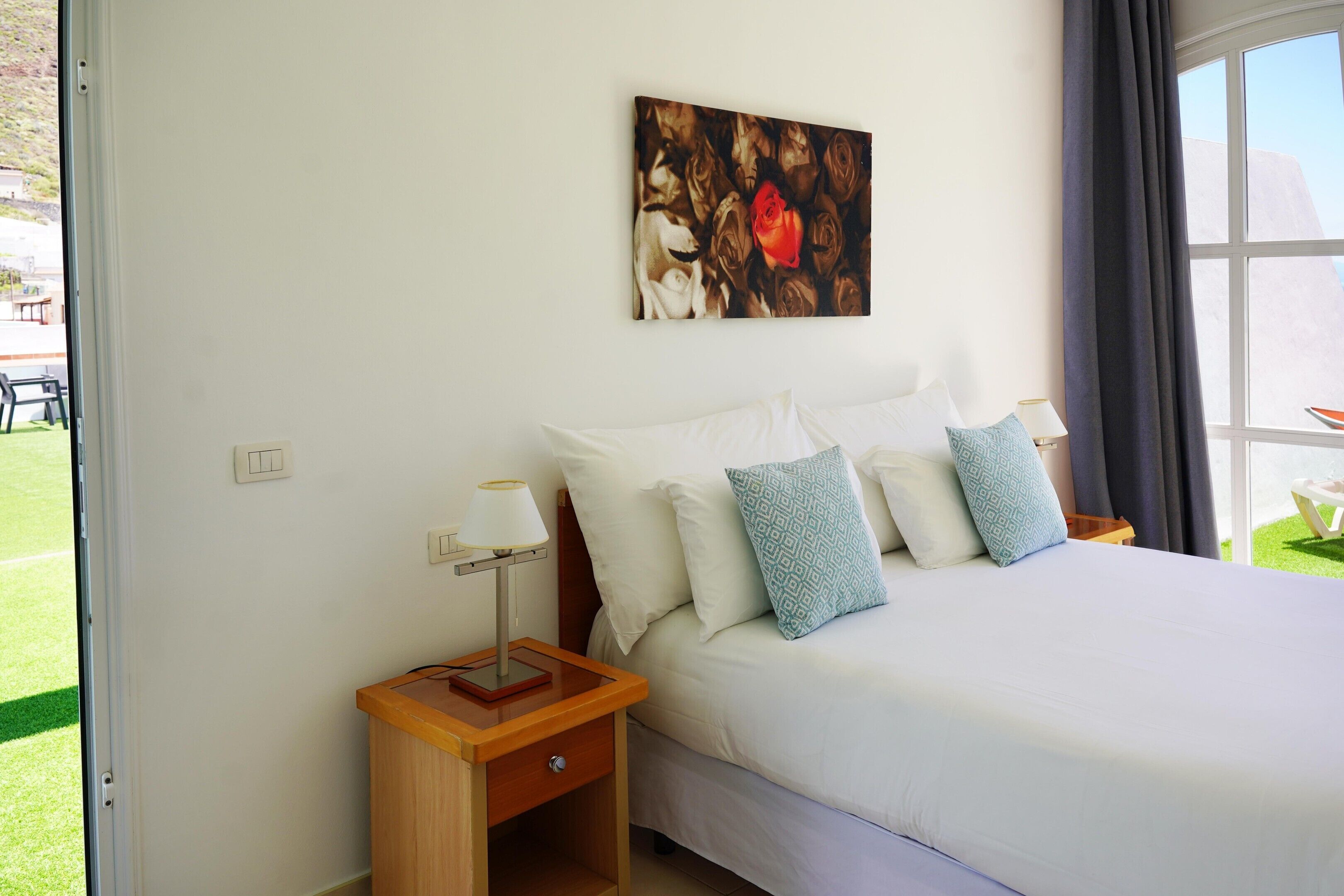 A hotel room with a bed, a nightstand, a lamp, and a painting on the wall.